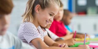 Mehrere Kinder sitzen an ihren Tischen in einem Klassenzimmer und schreiben in ihr Heft. 