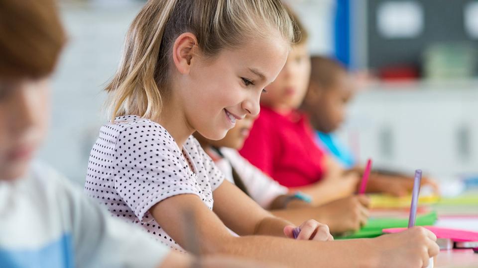 Mehrere Kinder sitzen an ihren Tischen in einem Klassenzimmer und schreiben in ihr Heft.
