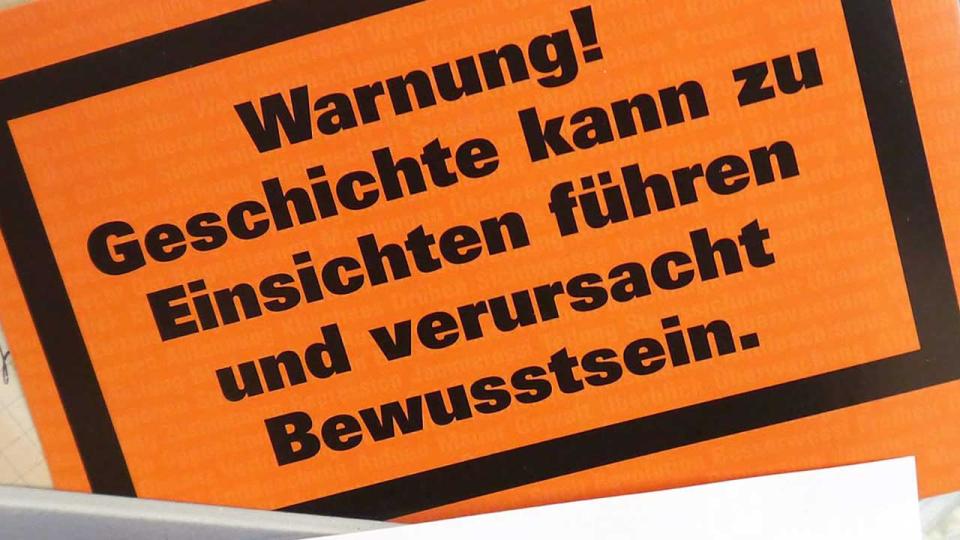 Oranges Schild mit der Aufschrift "Warnung! Geschichte kann zu Einsichten führen und verursacht Bewusstsein."