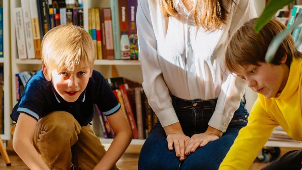 Vier lächelnde Kinder unterschiedlichen Alters, die in einer Bibliothek zusammen auf dem Boden sitzen. Team von Schülern, die in der Schule zusammenarbeiten und eine Strategie für ein zukünftiges Projekt planen.