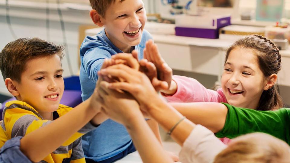 Gruppe glücklicher Kinder, die Roboter bauen und die Hände zusammenbringen