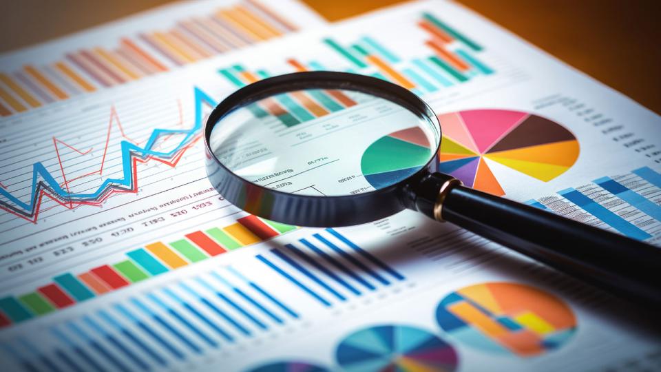 Gedruckte Geschäftsdokumente mit bunten Diagrammen und Grafiken, die durch ein Vergrößerungsglas analysiert werden