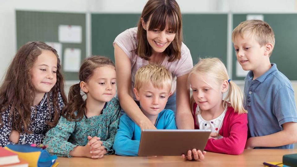 Lehrerin zeigt kleinen Kindern etwas am Tablet