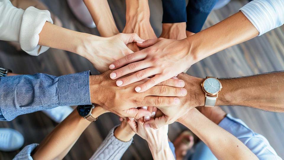 In der Draufsicht falten Menschen verschiedener Nationalitäten ihre Hände zusammen und symbolisieren so ihre Einigkeit und Unterstützung. Ein Team von Menschen, die für eine produktive Arbeit und ein positives Ergebnis bereit sind.