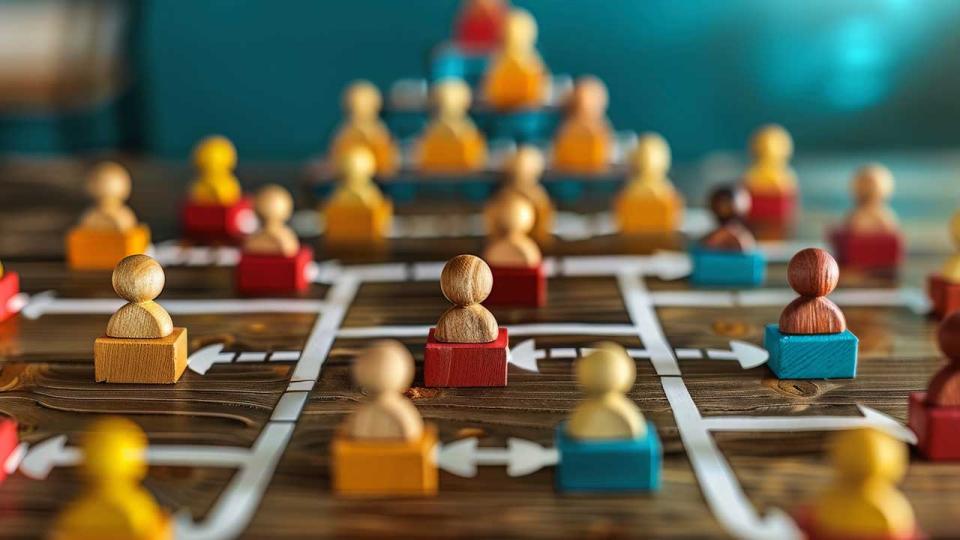 Ein Bild, das ein Holzbrett mit bunten Spielsteinen zeigt, die so angeordnet sind, dass sie ein komplexes Netzwerk oder eine Hierarchie darstellen, die wahrscheinlich eine soziale oder organisatorische Struktur symbolisieren. 