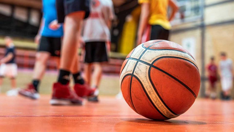 Ein Basketball auf dem Boden einer Sporthalle, unscharfe Füße von unbekannten Kindern