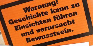 Oranges Schild mit der Aufschrift "Warnung! Geschichte kann zu Einsichten führen und verursacht Bewusstsein."
