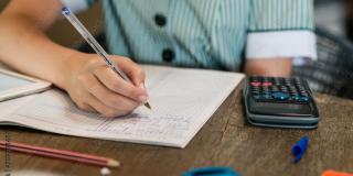 Schüler*in schreibt ins Schulheft, Taschenrechner, stifte und Schre liegen auf dem Tisch