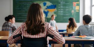 Konzept der inklusiven Bildung mit Rückansicht eines an den Rollstuhl gefesselten Schülers im Klassenzimmer.