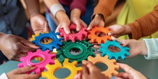 Verschiedene Charaktere versammeln sich um eine farbige Wand, die Inklusivität und Einheit in Wirtschaft und Finanzen, Teamwork und Zusammenarbeit symbolisiert.