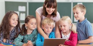 Lehrerin zeigt kleinen Kindern etwas am Tablet