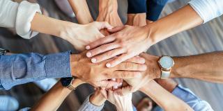 In der Draufsicht falten Menschen verschiedener Nationalitäten ihre Hände zusammen und symbolisieren so ihre Einigkeit und Unterstützung. Ein Team von Menschen, die für eine produktive Arbeit und ein positives Ergebnis bereit sind.