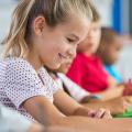 Mehrere Kinder sitzen an ihren Tischen in einem Klassenzimmer und schreiben in ihr Heft. 