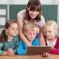 Lehrerin zeigt kleinen Kindern etwas am Tablet