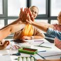 Lehrer und fröhliche Schüler feiern den erfolgreichen Abschluss einer gemeinsamen Schularbeit in einem hellen Klassenzimmer