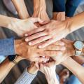 In der Draufsicht falten Menschen verschiedener Nationalitäten ihre Hände zusammen und symbolisieren so ihre Einigkeit und Unterstützung. Ein Team von Menschen, die für eine produktive Arbeit und ein positives Ergebnis bereit sind.